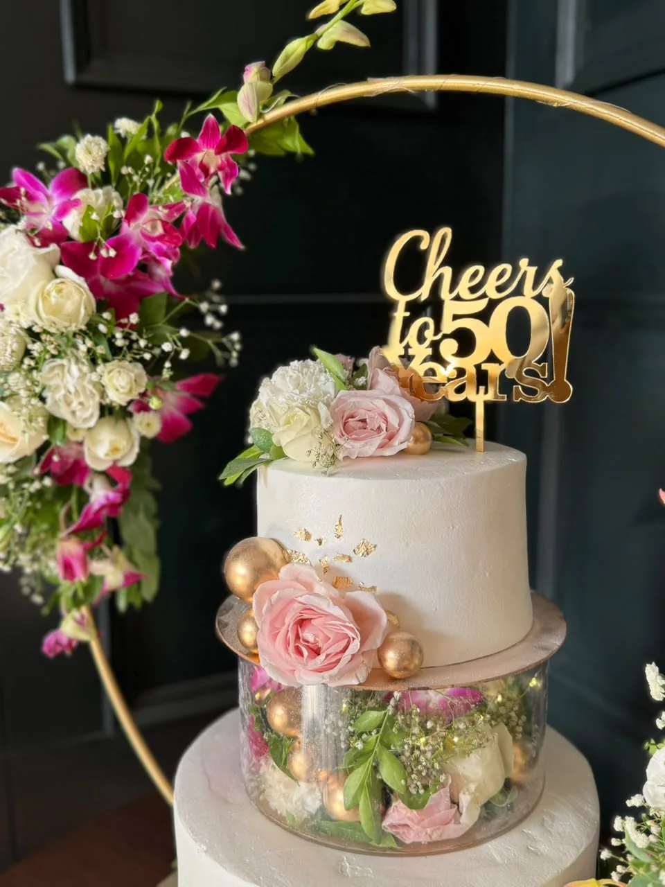 Floral two-tier anniversary cake with fresh roses and gold topper by Simply Sweet Udaipur
