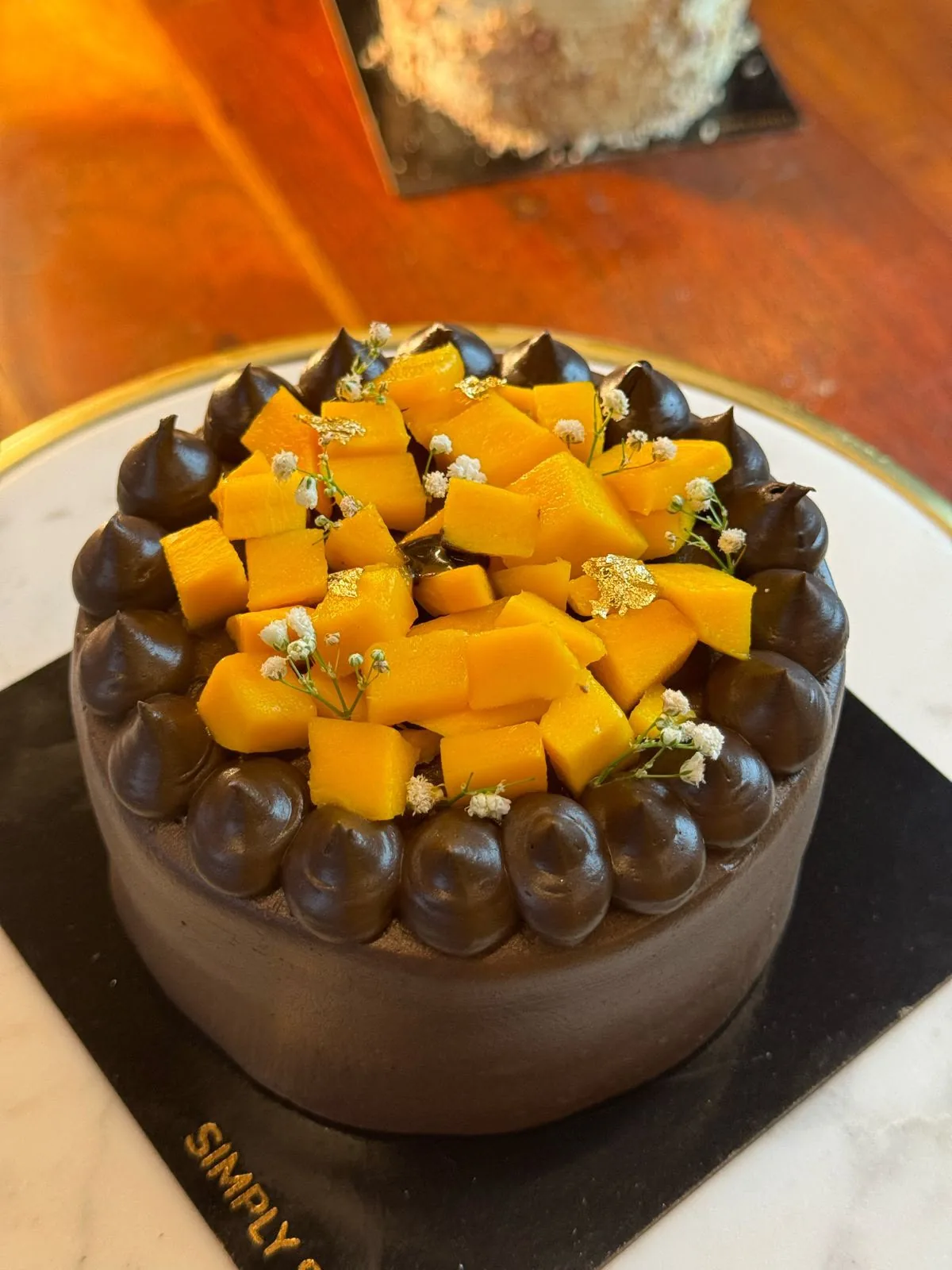 Eggless chocolate cake topped with fresh mango and edible gold by Simply Sweet Udaipur