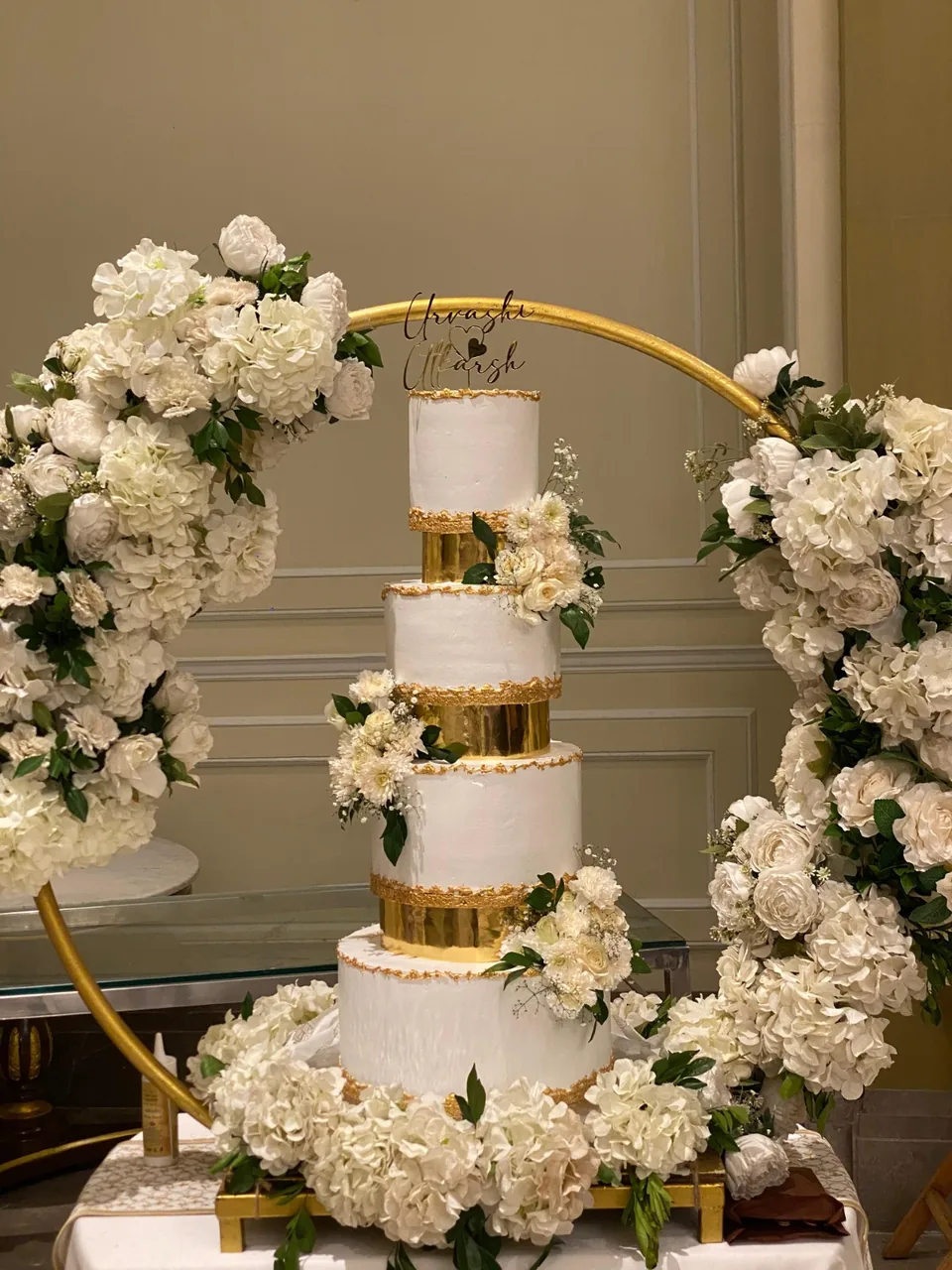 Five tier white and gold wedding cake framed by a floral hoop arch by Simply Sweet Udaipur