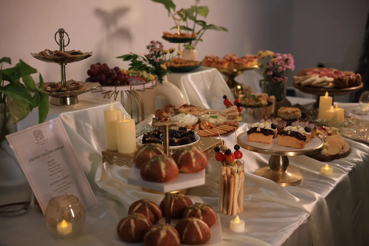 Grand grazing spread by Simply Sweet Udaipur with Korean-style garlic buns, breadsticks, dips, grapes, mini desserts and candles on tiered stands