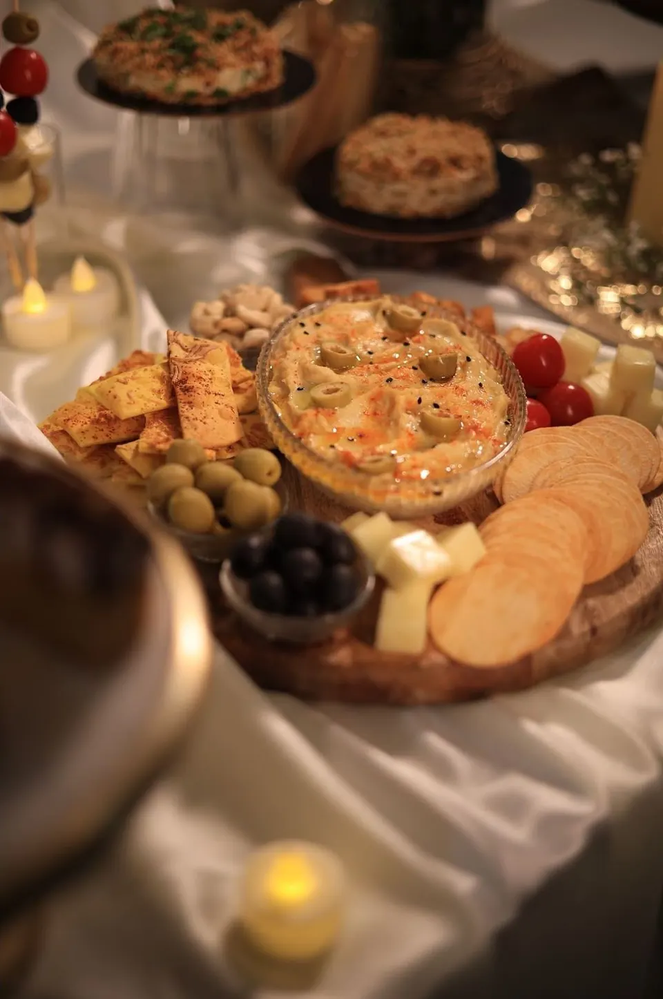 Hummus with olives, lavash crisps, crackers, cheese cubes and cherry tomatoes on a wooden platter at a Simply Sweet grazing table in Udaipur
